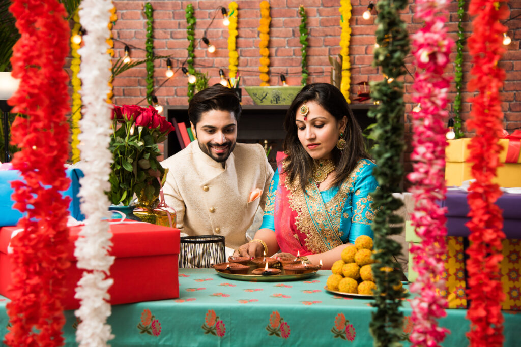 Why Traditional Celebrations Feel Meaningful When Planning Comes First indian couple with diya, sweets and gifts while celebrating diwali, deepavali or dipavali festival